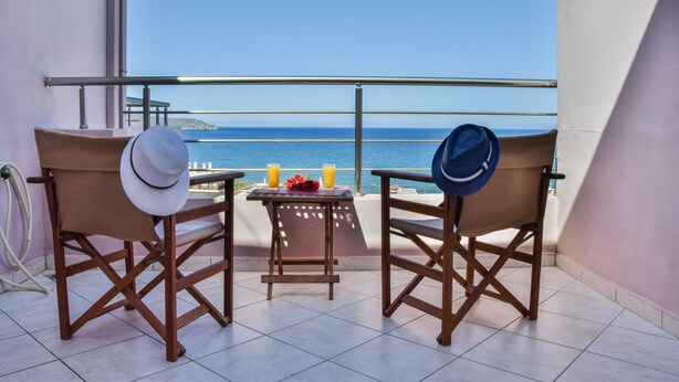 Two wooden chairs with hats, a small table with drinks, and a view of the sea.