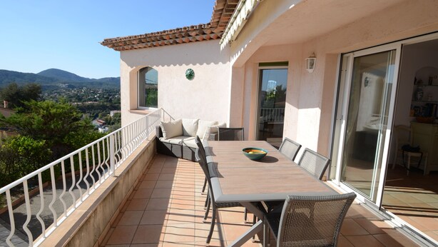 Eine Terrasse mit Esstisch und Stühlen, einer Sitzecke und einer Glastür zu einem Innenbereich.