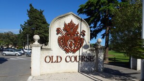 Ein Schild mit Wappen und dem Schriftzug 'OLD COURSE' an einer Gebäudefassade.