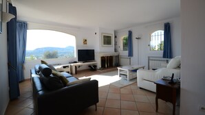 Ein Wohnzimmer mit einer Couch, einem weißen Sessel, einem Fernseher und einem Kamin.