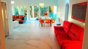 A spacious living area with a red sofa, a dining table with orange chairs, and a large window offering a view of trees. - "ALL NATURE"- Private Oasis.15km to airport. 25 km to Valencia. Sleeps 14+3 (El Rellano)