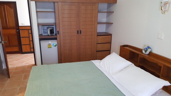 Un dormitorio con cama, un armario de madera, una pequeña kitchenette y una mesita de noche con un jarrón de flores.