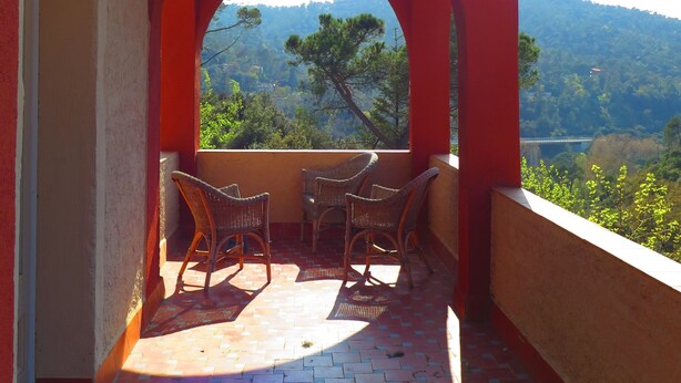 A balcony with a view of a mountainous landscape, furnished with wicker chairs and a tiled floor.
