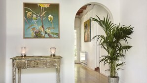 A hallway with a rustic wooden console table, two lit candles, a large potted plant, and a painting on the wall.
