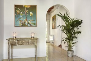 Um corredor com um console de madeira rústica, duas velas acesas, uma planta grande em vaso e um quadro na parede.