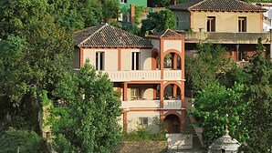 A multi-story building with a balcony, surrounded by lush greenery.