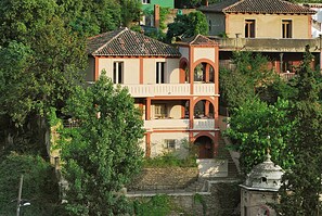 Um edifício de vários andares com varanda, rodeado por vegetação exuberante.
