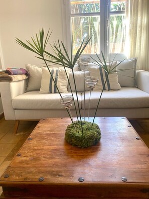 Sala de estar com sofá, mesa de centro com arranjo de musgo e janela com cortinas.