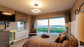 A bedroom with a large bed, a dresser, a chair, and a window with a view of the countryside. - Ocean Views ,kinsale 6 Bedroom house,sleeps 22,owned by Exquisite Holiday Homes  (Crohane , old head kinsale)