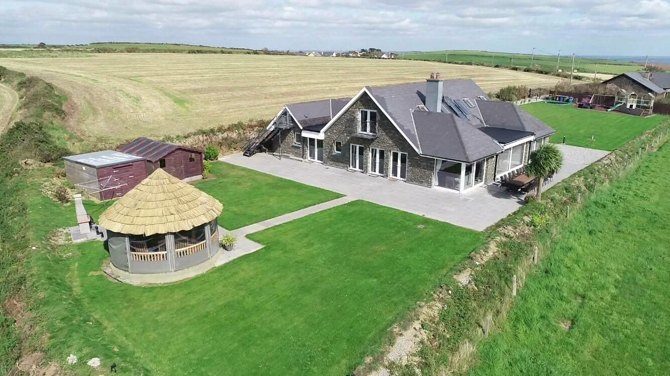 A large house with a spacious lawn, a circular structure with a thatched roof, and a barn.