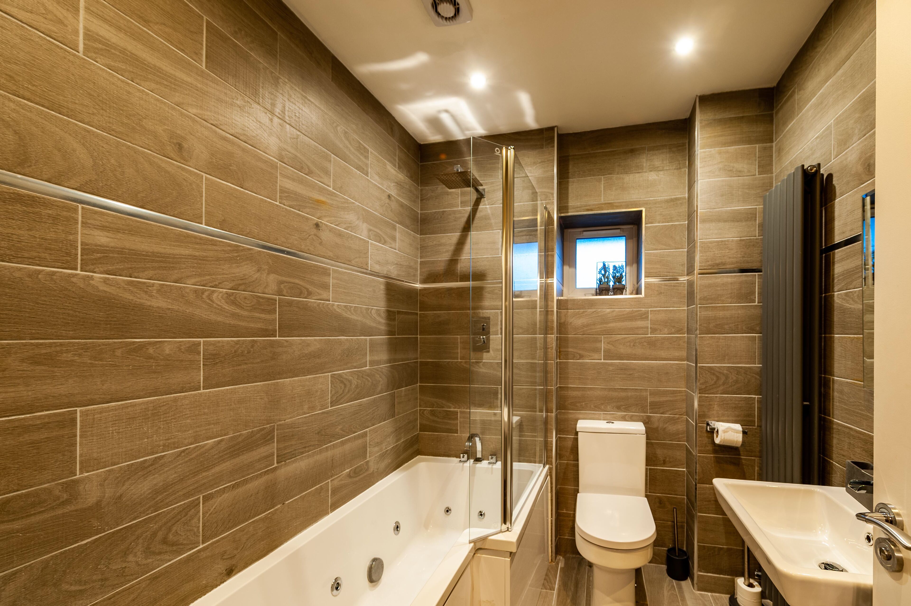 A modern bathroom with a wooden wall design, a glass-enclosed shower, a white bathtub, a toilet, and a sink.