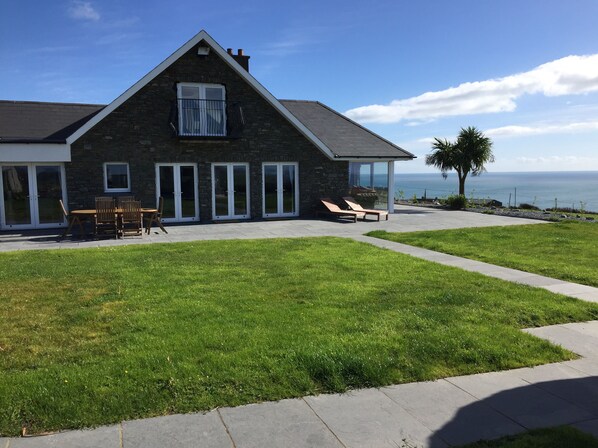 Ein Haus aus Stein mit Balkon, Rasen und Blick auf das Meer.