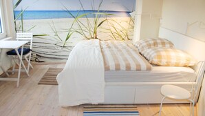 A bedroom with a bed, a chair, a desk, and a view of the beach. - Light-flooded apartment with private sauna! Beach walking distance, with dog! (Hohenkirchen)