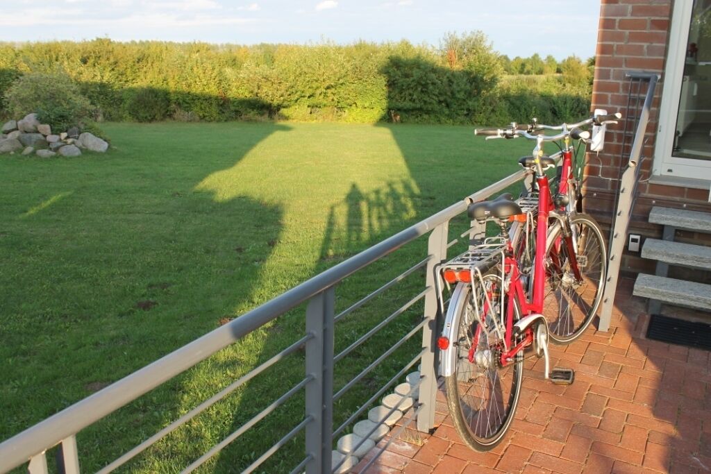 A red bicycle parked on a brick patio with a view of a grassy field and a hedge in the background.
