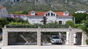 A two-story house with a red-tiled roof, a stone gate, and a car parked in front. - Apartment in Dubrovnik with swimming pool and sea view   (A1) (Dubrovnik Mokosica)