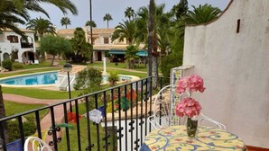 A balcony with a white metal chair and table, a small pool, and palm trees in the background.