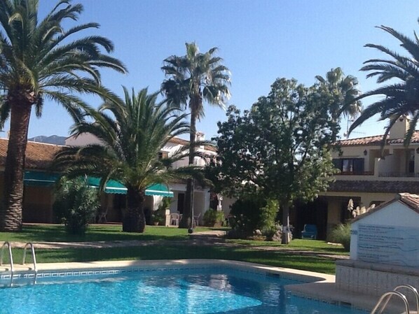 A swimming pool surrounded by palm trees and a building with a tiled roof. - Peaceful cottage, near the sea, close to Denia, family friendly (Dénia)