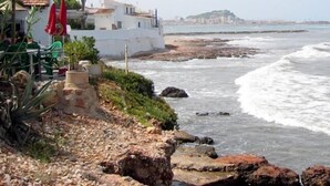 A coastal view with rocky terrain, a white building with red umbrellas, and a distant hill.