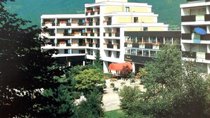 A multi-story hotel with balconies, surrounded by lush greenery and mountains in the background. - 2-room, internet, 3 beds, mountain view and garage (Bad Reichenhall)
