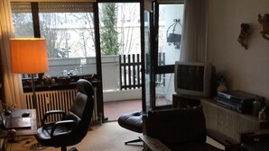 A living room with a sofa, a TV, a lamp, and a view of the outside. - 2-room, internet, 3 beds, mountain view and garage (Bad Reichenhall)