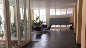 A spacious indoor area with a dark floor, large windows, and a seating area with chairs and a plant. - 2-room, internet, 3 beds, mountain view and garage (Bad Reichenhall)