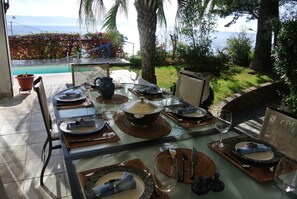 An outdoor dining area with a table set for a meal, overlooking a pool and a scenic view. -    Superb 5* family  Villa  for up to10 people (Ajaccio)