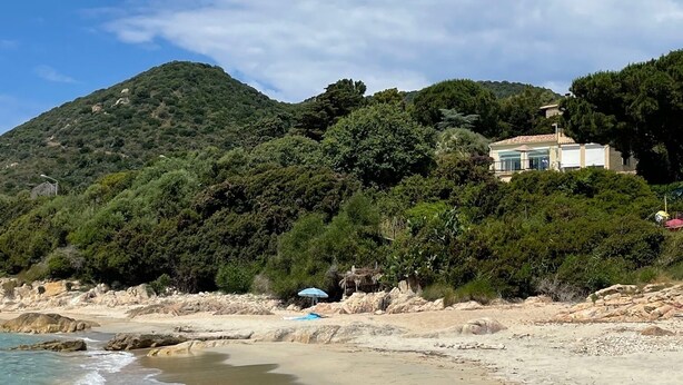 Una playa con una casa en una colina, cielos despejados y olas.