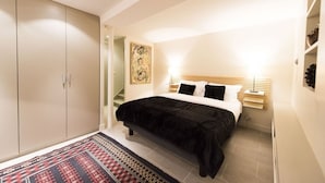 A bedroom with a bed, a wardrobe, a nightstand, a lamp, and a painting on the wall.