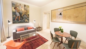 A living room with a sofa, coffee table, and chairs, a dining table with chairs, a painting on the wall, and a map.