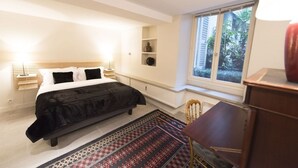A bedroom with a bed, bedside tables, a window, and a view of greenery outside.