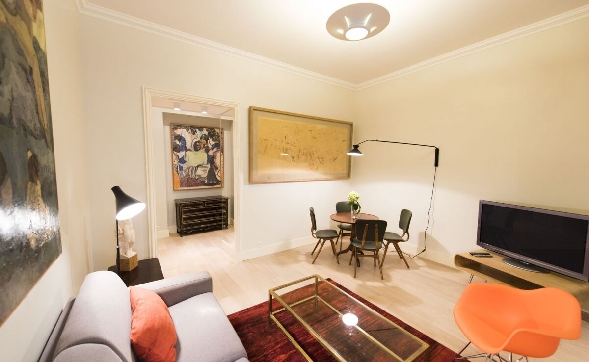 Una sala de estar moderna con un sofá, una mesa de comedor con sillas, un televisor y obras de arte en las paredes.