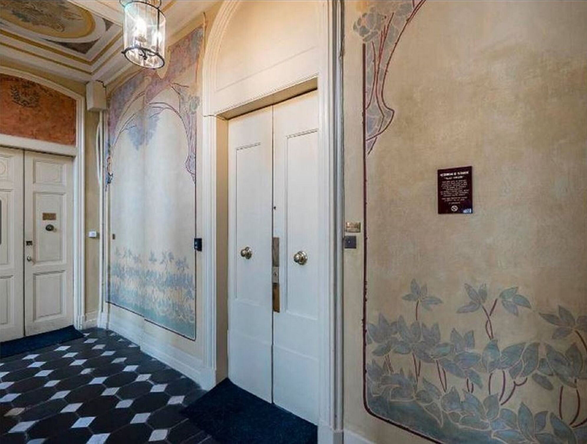 A hallway with a checkered floor, white doors, and decorative wall murals.