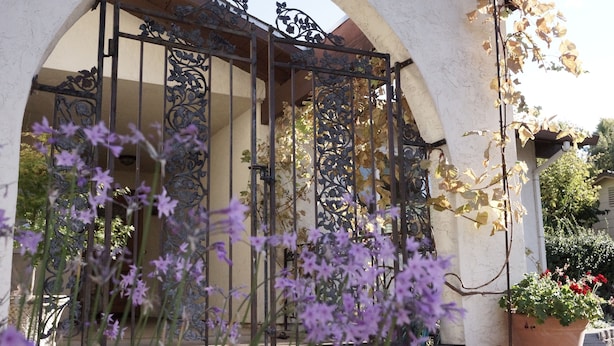 An ornate wrought iron gate with a floral design, leading to a building with a white facade and an arched entrance. - The Pineapple House -Best Reviews- Refreshing Swimming Pool! (Redding)