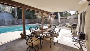 A covered patio with a pool, outdoor table and chairs, and a grill. - The Pineapple House -Best Reviews- Refreshing Swimming Pool! (Redding)