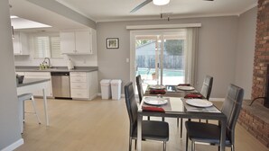 A modern kitchen with white cabinets, a dishwasher, and a dining area with a table set for four. - The Pineapple House -Best Reviews- Refreshing Swimming Pool! (Redding)