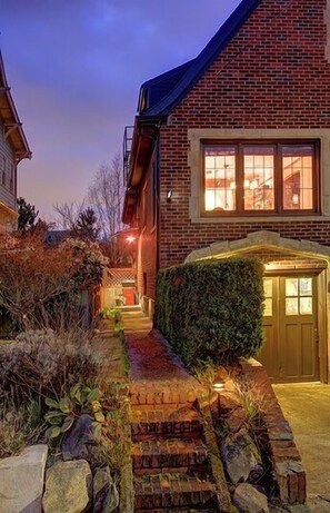 Een bakstenen huis met een goed verlichte entree, een kleine tuin en een pad van natuursteen dat naar de deur leidt.