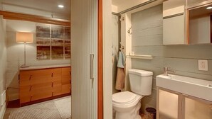 Une salle de bain avec des toilettes, un lavabo et un miroir. Une serviette est accrochée au mur et une lampe est posée sur le sol.