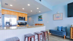 Une cuisine moderne avec des meubles en bois, des appareils électroménagers en acier inoxydable et un coin bar avec des tabourets.