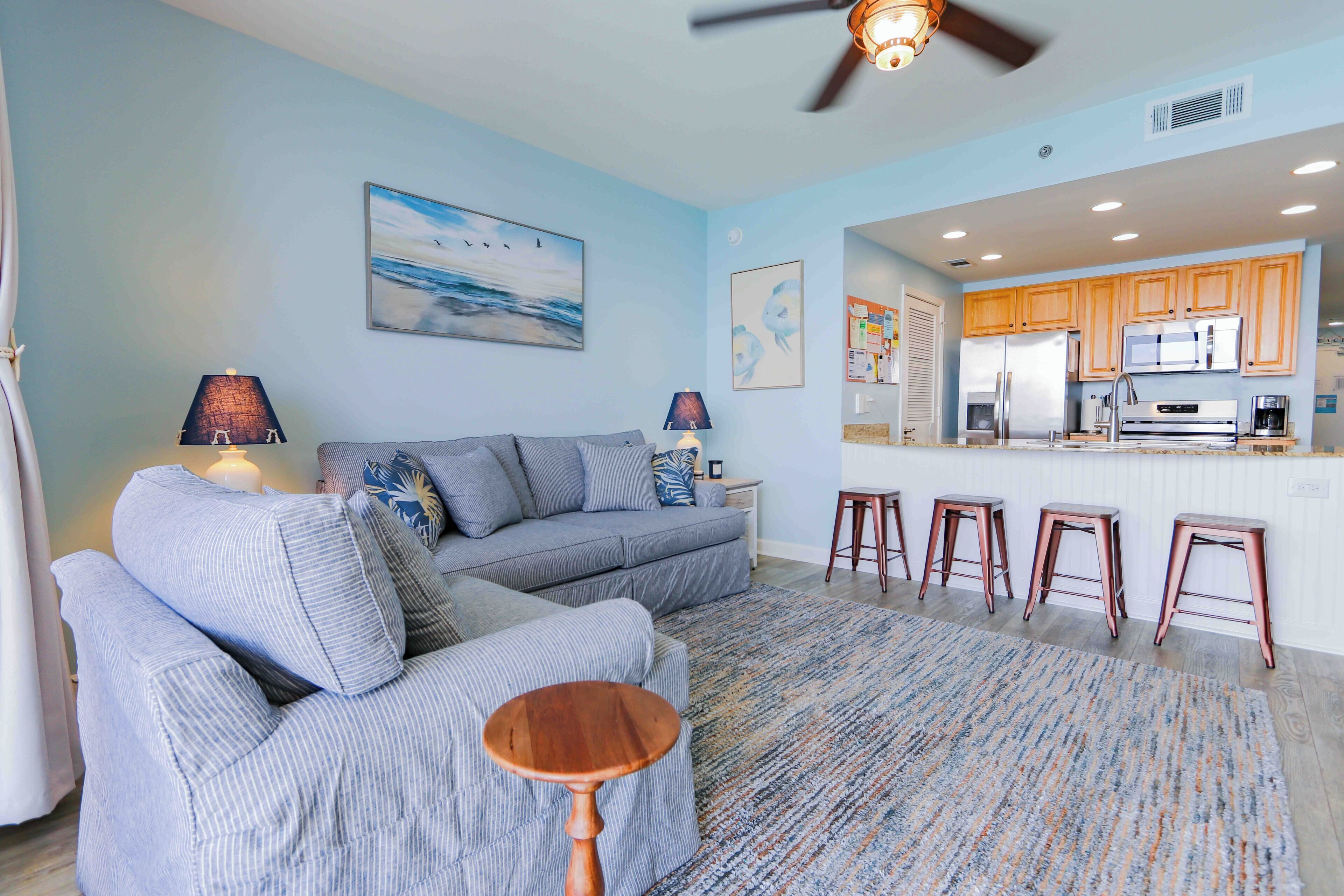 A living room with a sofa, a coffee table, and a kitchen area with a refrigerator and bar stools.