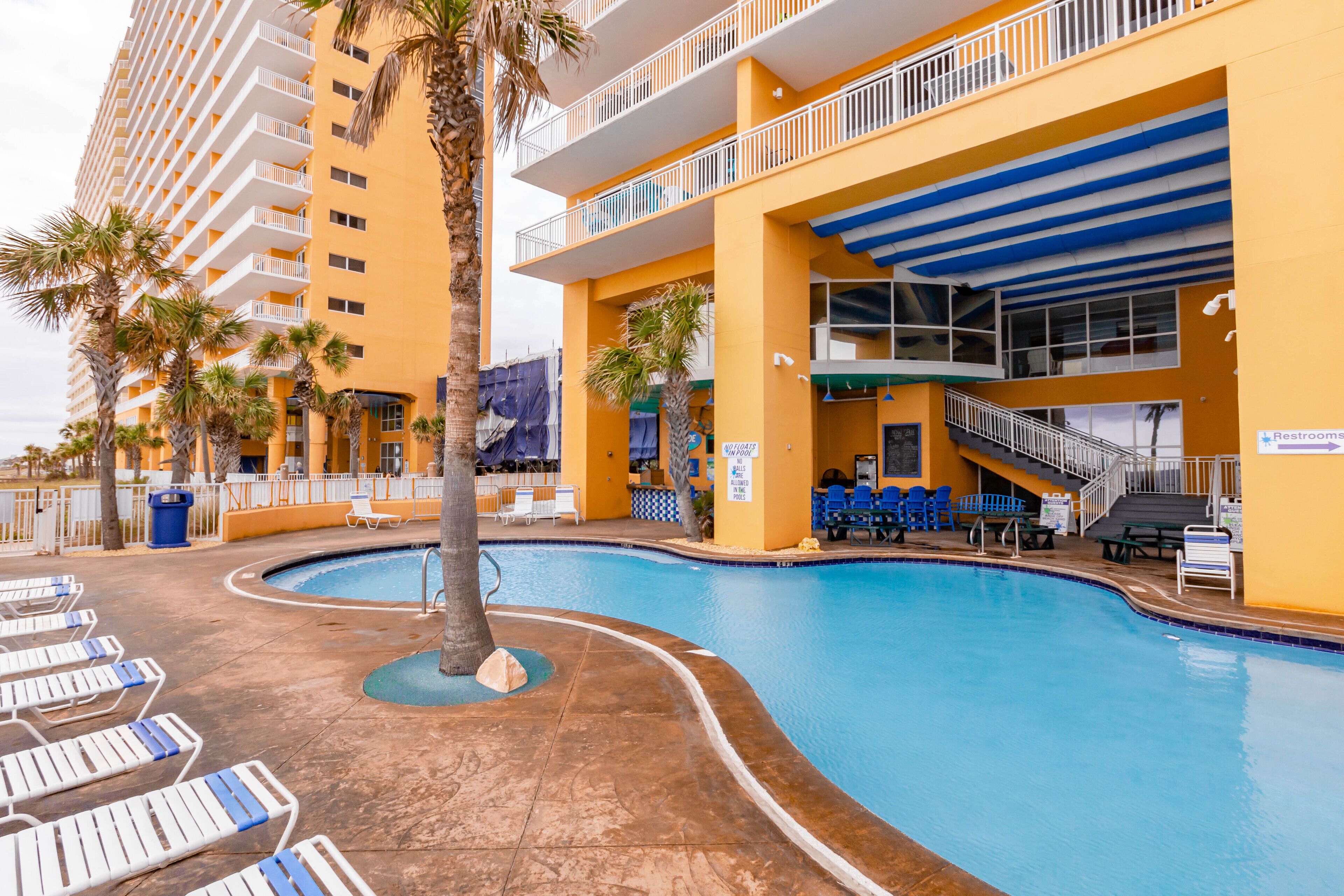 A hotel with a pool area, including lounge chairs, a staircase, and a sign indicating restrooms.