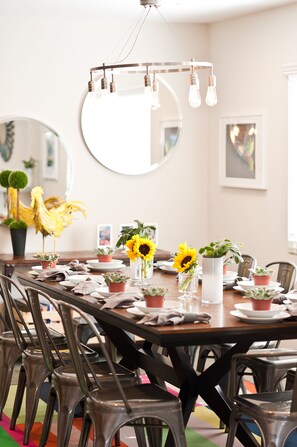 A dining area with a round table set for six, surrounded by metal chairs. There are potted plants on the table, and a chandelier hangs above. - LAST MINUTE SPECIAL! Amenities! Pool & Game Room! Close walk to Disney! (Anaheim)