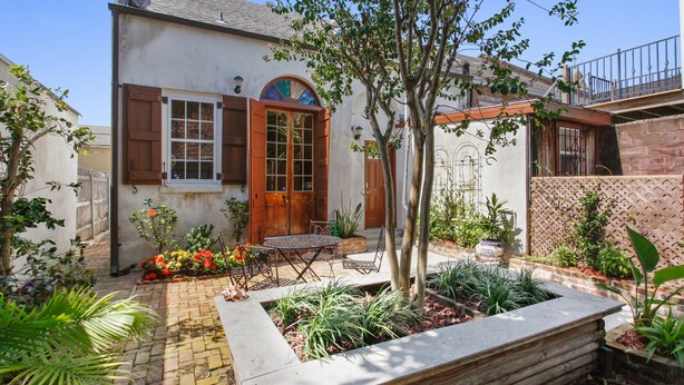 A house with a wooden door, a small patio with a table and chairs, and a garden with various plants.