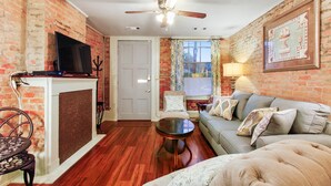 A living room with a fireplace, a television, a sofa, and a ceiling fan.