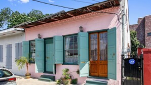 A pink building with teal shutters, a wooden door, and a black gate.