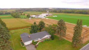 Et landligt landskab med et stort hus omgivet af marker, et silosilo og en lade.
