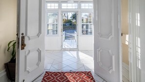 A white door with a red patterned rug leading to a balcony with a view of trees and a garden.