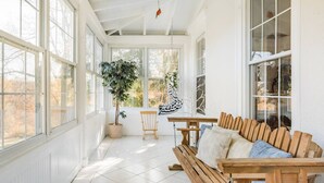 A sunlit room with a wooden bench, a hanging chair, and a potted plant.