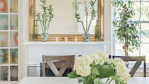 A dining area with a large table, chairs, a chandelier, a mirror, and potted plants.