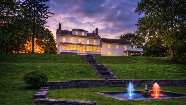 A large, two-story house with a well-maintained lawn and a stone staircase leading to the entrance.