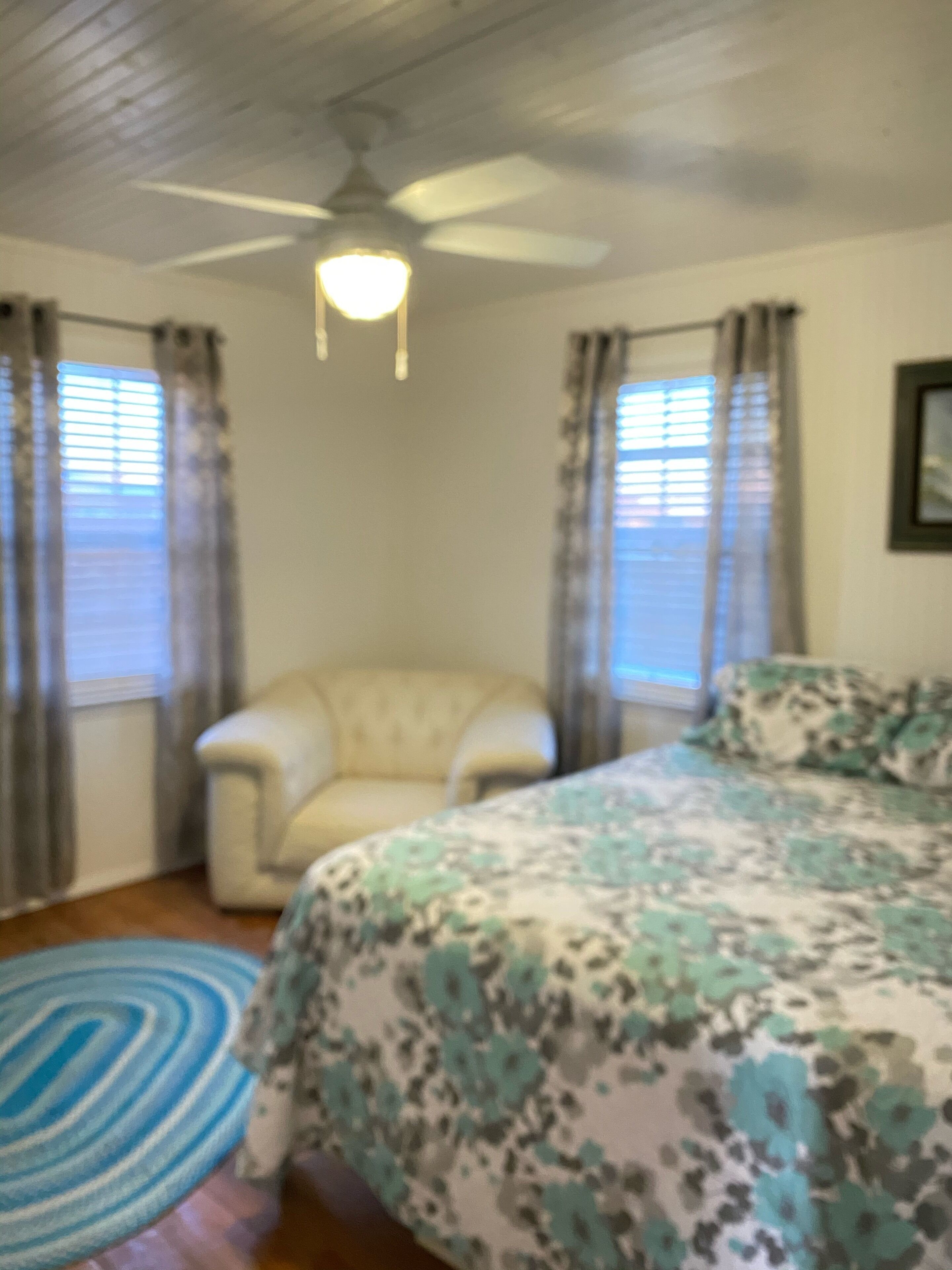 A bedroom with a bed, a chair, a ceiling fan, and a window with curtains.